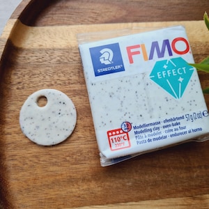 May include: A package of FIMO Effect modeling clay, a white clay with black flecks, in a white and blue package with the text "FIMO EFFECT" and "Modelliermasse ofenhärtend 57g (2oz) e". The package also includes the text "110°C 230°F" and "30".