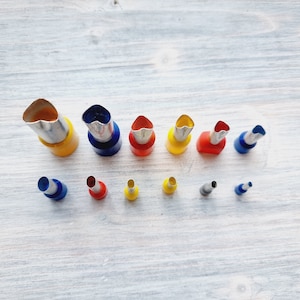 May include: A set of 13 metal flower-shaped cookie cutters in various sizes. The cutters are arranged in two rows, with the larger cutters in the top row and the smaller cutters in the bottom row. The cutters are yellow, red, and blue.