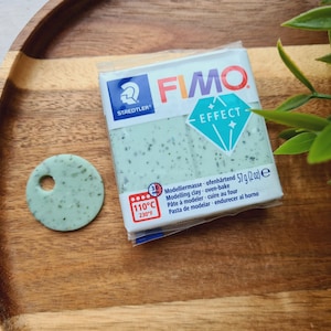 May include: A package of FIMO Effect modeling clay in a green speckled color. The package has the text "FIMO EFFECT" and "Modellermasse ofenhärtend 57 g (2 oz) e" on it. The clay is oven-bake and can be used for crafting.