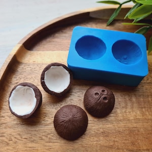Peut inclure: Un moule en silicone bleu pour faire deux bonbons en forme de noix de coco. Quatre bonbons en forme de noix de coco bruns sont également présentés sur une surface en bois.
