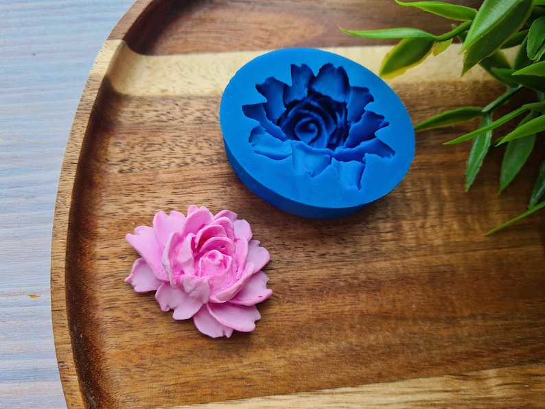 May include: A blue silicone mould for making a pink flower shaped cake decoration. The mould is on a wooden surface.