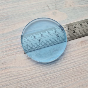 Puede incluir: Un círculo de vidrio transparente de 5 cm de diámetro, con una regla colocada encima.