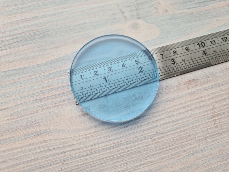 May include: A clear glass circle measuring 2 inches in diameter, with a ruler placed on top of it.