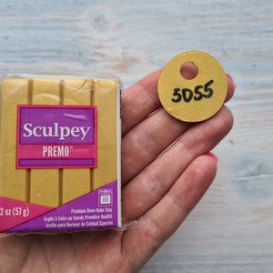 Könnte beinhalten: Eine 57 Gramm Packung goldfarbener Sculpey Premo Backofen-Modelliermasse. Die Verpackung hat ein Etikett mit dem Markennamen, dem Produktnamen und Gebrauchsanweisungen. Ein goldenes Etikett mit der Nummer 5055 ist ebenfalls sichtbar.