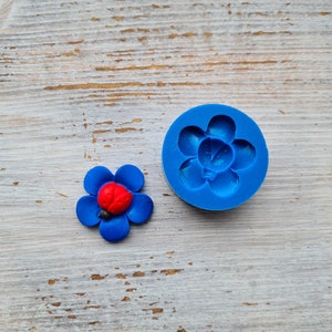 Könnte beinhalten: Eine blaue Silikonform in Form einer Blume mit einem Marienkäfer in der Mitte. Neben der Form befindet sich eine blaue Blume mit einem Marienkäfer in der Mitte.