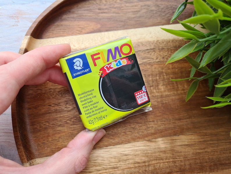 May include: A black FIMO Kids oven-bake modelling clay in a 1.5 ounce package. The package has a yellow background with the FIMO Kids logo and the text "Modelliernusse ofenh&auml;rtend Modelling clay oven-bake P&acirc;te &agrave; modeler cuire au four Pasta de modelar endurence al horno 42g (1.5oz) e MADE IN GERMANY FABRIQUE EN ALLEMAGNE".