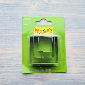 Könnte beinhalten: Ein Satz mit drei quadratischen Ausstechern in einer grünen Plastikverpackung. Die Verpackung trägt den Text "Makin's" in gelben Buchstaben. Die Ausstecher sind ineinander verschachtelt, wobei der größte Ausstecher der äußerste ist.