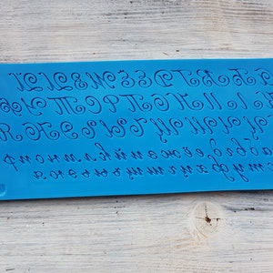 May include: Blue silicone baking mat with a raised alphabet in a cursive font. The letters are uppercase and include A through Z.