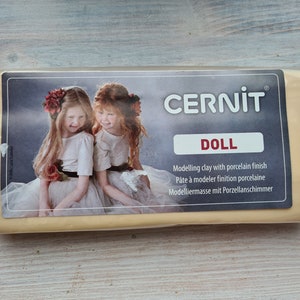 May include: A package of yellow modeling clay labeled "CERNIT DOLL" with a porcelain finish. The package features a photo of two young girls with red flowers in their hair.