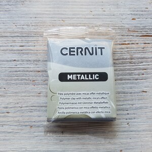Puede incluir: Un paquete de arcilla polim&eacute;rica met&aacute;lica de la marca Cernit. El paquete es plateado y tiene el texto "CERNIT METALLIC" en la parte delantera. El texto "P&acirc;te polym&egrave;re avec micas effet m&eacute;tallique Polymer clay with metallic mica's effect Polymermasse mit Glimmer-Metalleffekt Pasta polimerica con mica effetto metallico Arcilla polimerica met&aacute;lica con efecto mica" est&aacute; impreso en la parte posterior.