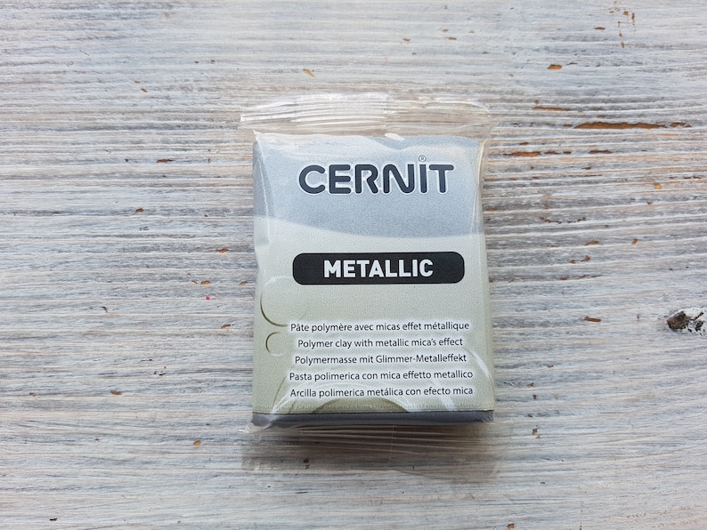 Puede incluir: Un paquete de arcilla polim&eacute;rica met&aacute;lica de la marca Cernit. El paquete es plateado y tiene el texto "CERNIT METALLIC" en la parte delantera. El texto "P&acirc;te polym&egrave;re avec micas effet m&eacute;tallique Polymer clay with metallic mica's effect Polymermasse mit Glimmer-Metalleffekt Pasta polimerica con mica effetto metallico Arcilla polimerica met&aacute;lica con efecto mica" est&aacute; impreso en la parte posterior.