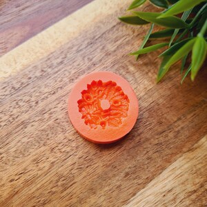 Puede incluir: Molde de silicona naranja con un dise&ntilde;o floral. El molde tiene forma de c&iacute;rculo con un agujero en el centro.