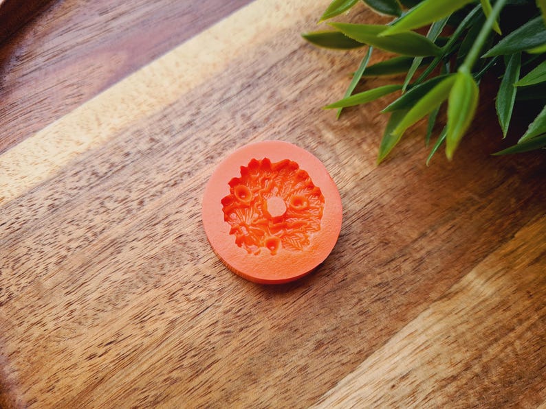 Puede incluir: Molde de silicona naranja con un dise&ntilde;o floral. El molde tiene forma de c&iacute;rculo con un agujero en el centro.