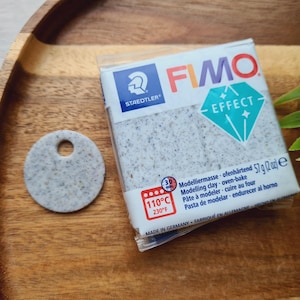 May include: A package of FIMO Effect modeling clay, a white and gray speckled clay with a diamond-shaped logo. The package is labeled with the text "FIMO Effect" and "Staedtler". The package also includes instructions for baking the clay at 110°C (230°F).