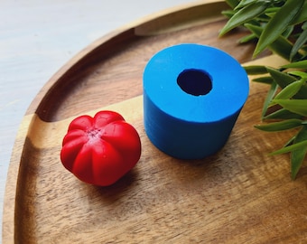 May include: A red, round, textured silicone mold for making a small, round cake or dessert. The mold is sitting on a wooden surface next to a blue silicone mold with a hole in the center.