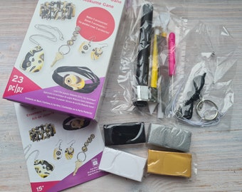 May include: A craft kit for making jewelry using the Mokume Gane technique. The kit includes four colors of clay, a tool for shaping the clay, and a small key chain. The box is pink and purple with the text "Mokume Gane" and "23 pc/pz".