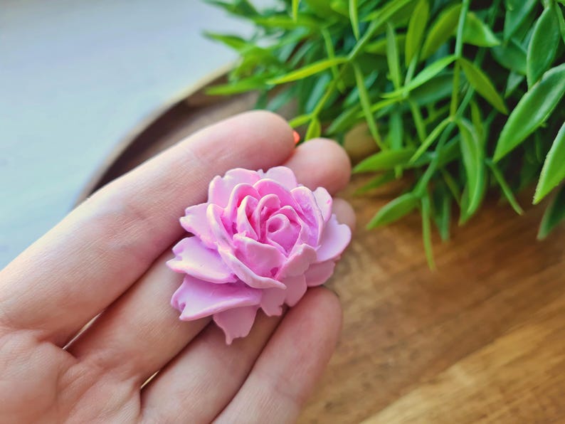 May include: A pink, handmade, polymer clay rose flower. The rose is detailed with multiple layers of petals.