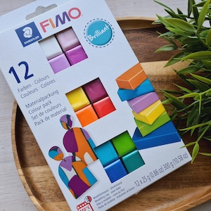 May include: A pack of 12 FIMO modelling clay colours in a range of bright shades. The pack contains 12 individual 25 gram blocks of clay. The packaging is labelled "Brilliant" and "12 Farben - Colours - Couleurs - Colores".