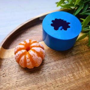May include: A blue silicone mold shaped like a flower with a small orange citrus fruit next to it on a wooden tray.