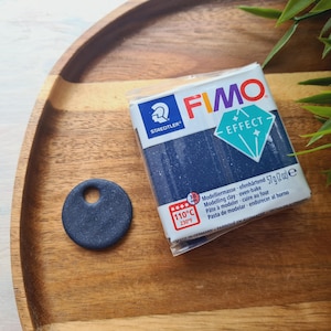 May include: A package of FIMO Effect modeling clay in a dark blue color with a sparkly finish. The package has the text "FIMO Effect" and "110°C 230°F" printed on it.