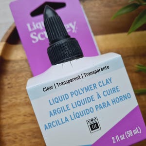 May include: A 2-ounce bottle of clear liquid polymer clay. The bottle has a black cap and a label that says "Liquid Polymer Clay, Argile Liquide &agrave; Cuire, Arcilla L&iacute;quido Para Horno".