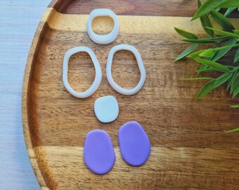 May include: A set of five white silicone molds for crafting, including two oval shapes, one round shape, and two smaller square shapes. Two purple clay shapes are also included.
