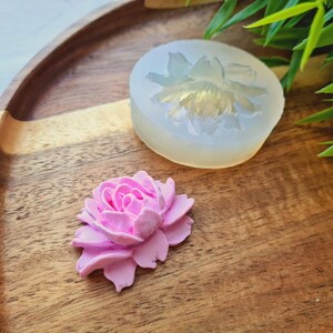 May include: A pink polymer clay flower, next to a silicone mould of a flower. The mould is clear and shows the details of the flower.