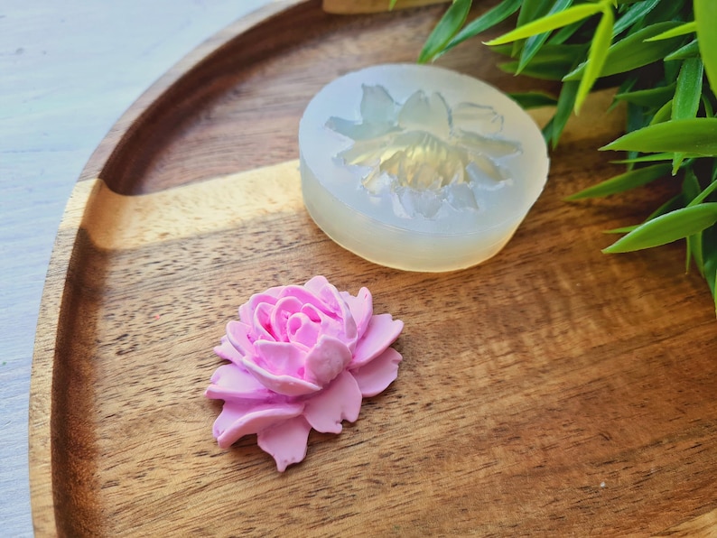 May include: A pink polymer clay flower, next to a silicone mould of a flower. The mould is clear and shows the details of the flower.