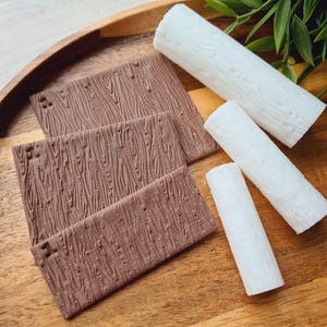 Può includere: Un vassoio di legno contiene diversi pezzi rettangolari marroni con una texture a venature del legno, insieme a pezzi cilindrici bianchi. Gli oggetti sono disposti su un vassoio di legno, con fogliame verde sullo sfondo. Gli oggetti sembrano decorativi o per l'artigianato.
