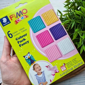 May include: A box of FIMO kids modeling clay in a fancy color pack. The box features six colors of clay: teal, gold, purple, pink, light pink, and white. The box also includes a picture of an owl and a unicorn.