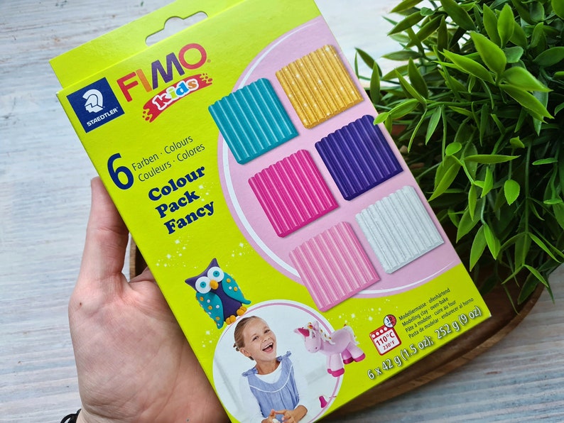 May include: A box of FIMO kids modeling clay in a fancy color pack. The box features six colors of clay: teal, gold, purple, pink, light pink, and white. The box also includes a picture of an owl and a unicorn.