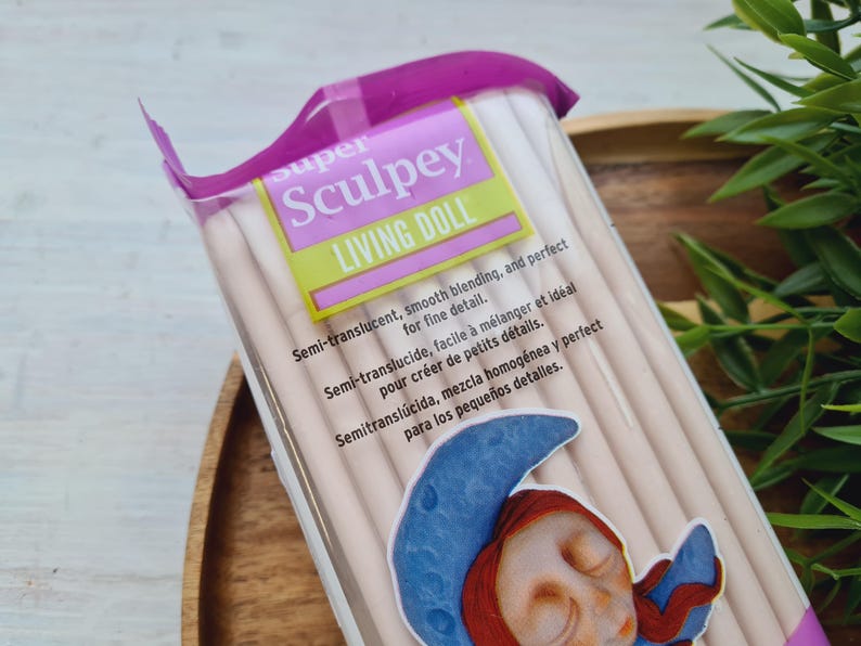 May include: A package of Super Sculpey Living Doll polymer clay. The package is pink and white with the text "super Sculpey Living Doll" on the front. The text on the package reads "Semi-translucent, smooth blending, and perfect for fine detail. Semi-translucide, facile &agrave; m&eacute;langer et id&eacute;al pour cr&eacute;er de petits d&eacute;tails. Semitransl&uacute;cida, mezcla homog&eacute;nea y perfect para los peque&ntilde;os detalles."