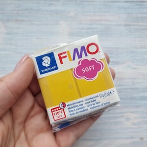 May include: A pack of yellow FIMO Soft modelling clay. The pack is white with the FIMO logo and the words "Soft" and "Staedtler". The pack also includes instructions for baking the clay at 110 degrees Celsius or 230 degrees Fahrenheit.