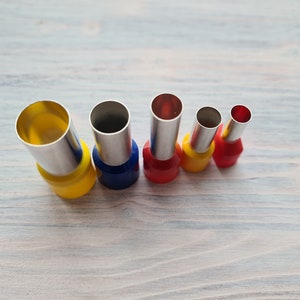 May include: Set of five wire crimping tools with different sized openings. The tools are made of metal with a silver finish and have colored plastic handles. The handles are yellow, blue, red, yellow, and red.