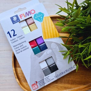 May include: A pack of 12 FIMO Effect polymer clay colours. The pack includes 6 colours of FIMO Effect clay and 6 colours of FIMO clay. The pack is labelled with the brand name FIMO and the text "12 Farben Colours Couleurs Colores Materialpackung Colour pack Set de couleurs Pack de material".