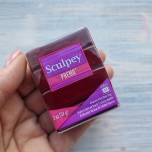 Peut inclure: Un petit paquet rectangulaire d'argile à cuire au four Sculpey Premo. Le paquet est violet, rose et blanc avec le nom de la marque et le nom du produit imprimés dessus. Le paquet fait 2 onces (57 grammes).