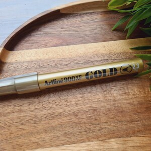 Marcador de tinta metálica Artline 900XF, DORADO, 2,3 MM, ideal para decorar y escribir sobre cartón, plástico, vidrio, metal o cerámica.