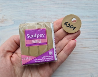 May include: A package of Sculpey Soufflé polymer clay, 1.7 oz (48 g), in a tan color. A small, round, tan clay piece with the number 6301 written on it. The packaging has a pink and purple label.
