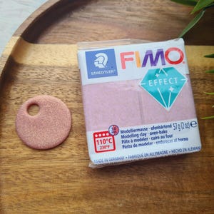 May include: A pack of FIMO Effect modelling clay in a pink colour with a glittery finish. The pack has the text "STAEDTLER" and "FIMO EFFECT" on it. The pack also includes instructions for using the clay, including the baking temperature of 110°C (230°F).