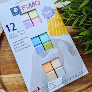 May include: A pack of 12 FIMO modelling clay colours in pastel shades. The pack includes 12 individual 25 gram blocks of clay in colours such as light blue, light green, light pink, and light yellow. The pack is labelled "FIMO Pastel" and "12 Farben. Colours. Couleurs. Colores."