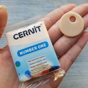 May include: A package of white opaque polymer clay labeled "CERNIT NUMBER ONE" with a small round disc of the same clay with a hole in the center.