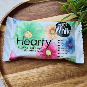 Może przedstawiać: Opakowanie białej modeliny Hearty Super Lightweight. Opakowanie zawiera wzór kwiatowy i napis "White" w kółku. Opakowanie zawiera również instrukcje w języku japońskim.