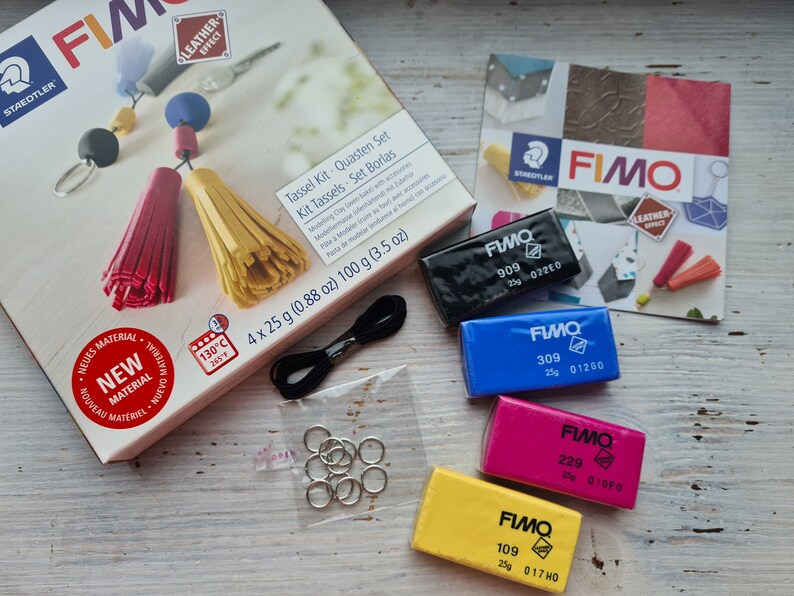 May include: A Fimo Tassel Kit with four 25 gram blocks of polymer clay in black, blue, pink, and yellow. The kit also includes black string, silver jump rings, and instructions for making tassels. The box reads "Tassel Kit - Quasten Set - Kit Tassels - Set Borlas".