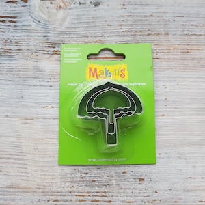 May include: A set of three metal cookie cutters shaped like umbrellas. The cutters are packaged on a green card with the Makin's Clay logo and website address.