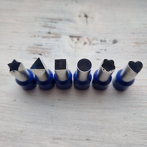 May include: Set of seven metal cookie cutters with blue handles. The cutters are shaped like a star, triangle, square, circle, flower, and heart.