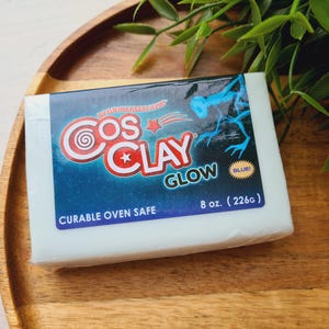 Puede incluir: Un paquete rectangular blanco de CosClay Glow, un producto de arcilla polimérica. El paquete presenta un logotipo azul y rojo con el texto "CosClay Glow" y "Blue!". El paquete pesa 226g y es apto para horno.