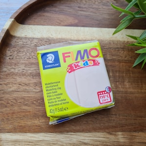 May include: A package of FIMO Kids oven-bake modeling clay, 42g (1.5 oz), in a light beige color. The package is yellow and features the Staedtler logo and the text "FIMO Kids". The clay is oven-bake at 230°F (110°C).