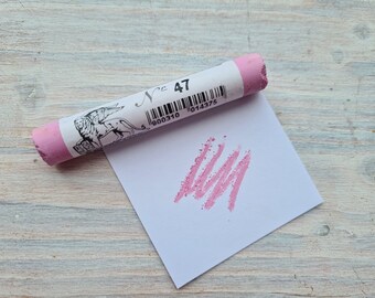 May include: A pink pastel stick with a white label that says "N° 47" and a barcode. The stick is lying on a white piece of paper with a pink pastel stroke on it.