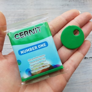 May include: A package of green polymer clay labeled "CERNIT NUMBER ONE" with the text "Pâte polymère opaque, Opaque polymer clay, Opake Polymermasse, Pasta Polimerica opаса, Arcilla polimerica oрасо" and a small green circle with a hole in the center.
