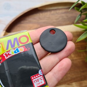 May include: A black FIMO Kids modelling clay package with the text "FIMO Kids" and "110&deg;C 230&deg;F" on the front. A black clay circle with a hole in the centre is shown in the background.